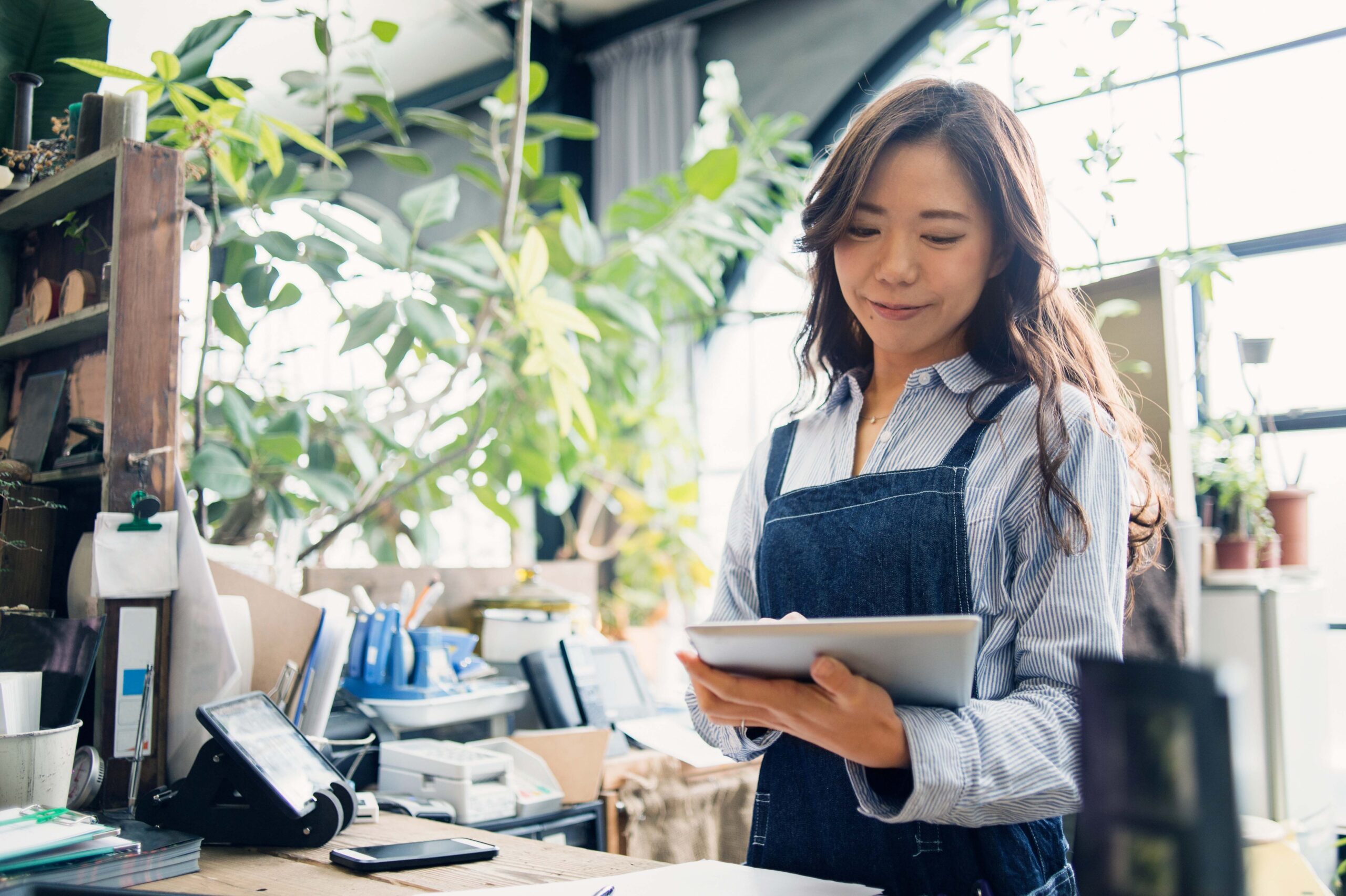A woman works on her small business. She's wearing an apron and smiling while using an iPad to explore financing solutions.