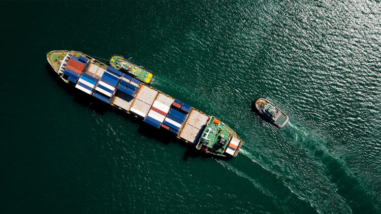 A container ship sails across a green sea.